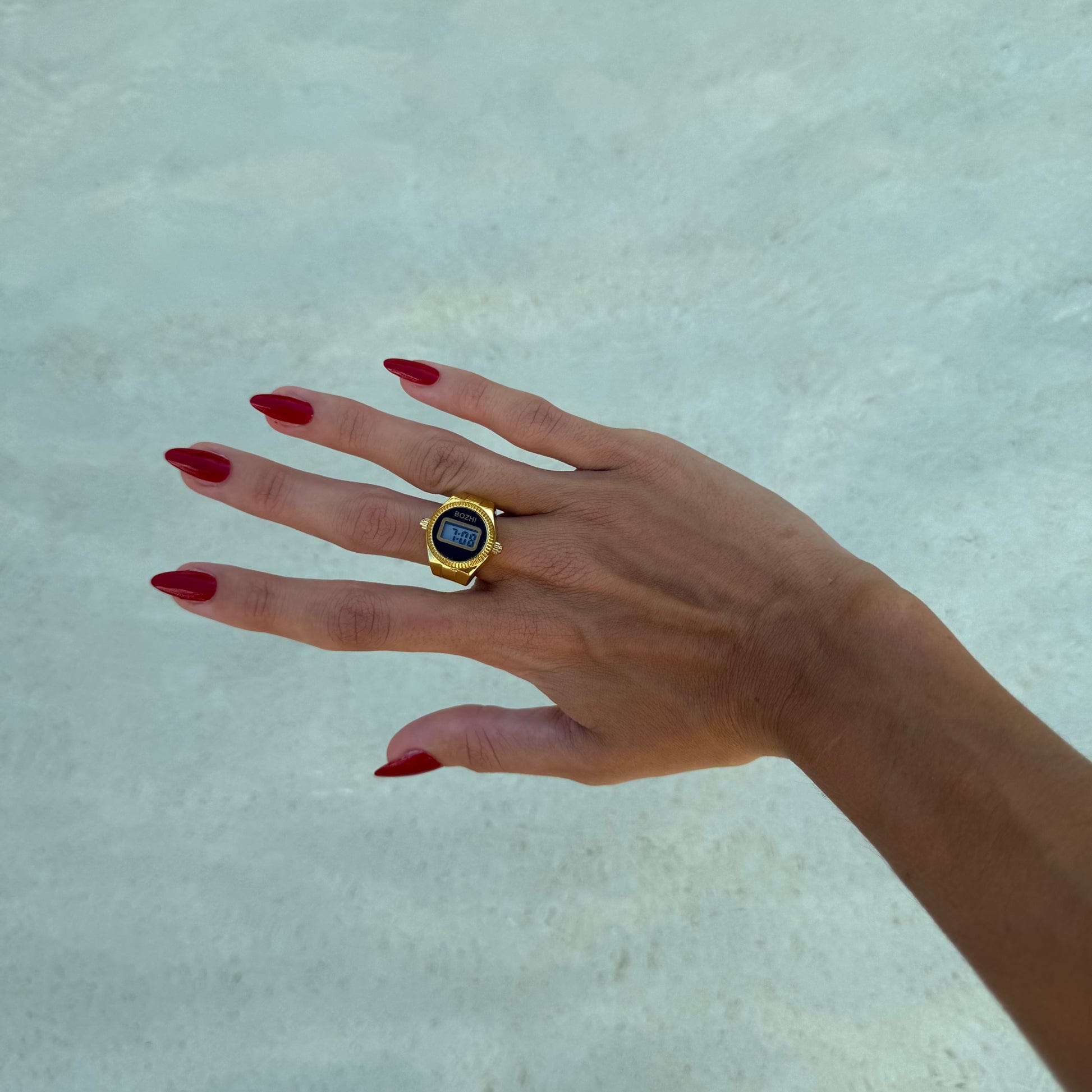 Bague Montre Dorée - Cadran Digital Noir portée sur un majeur féminin